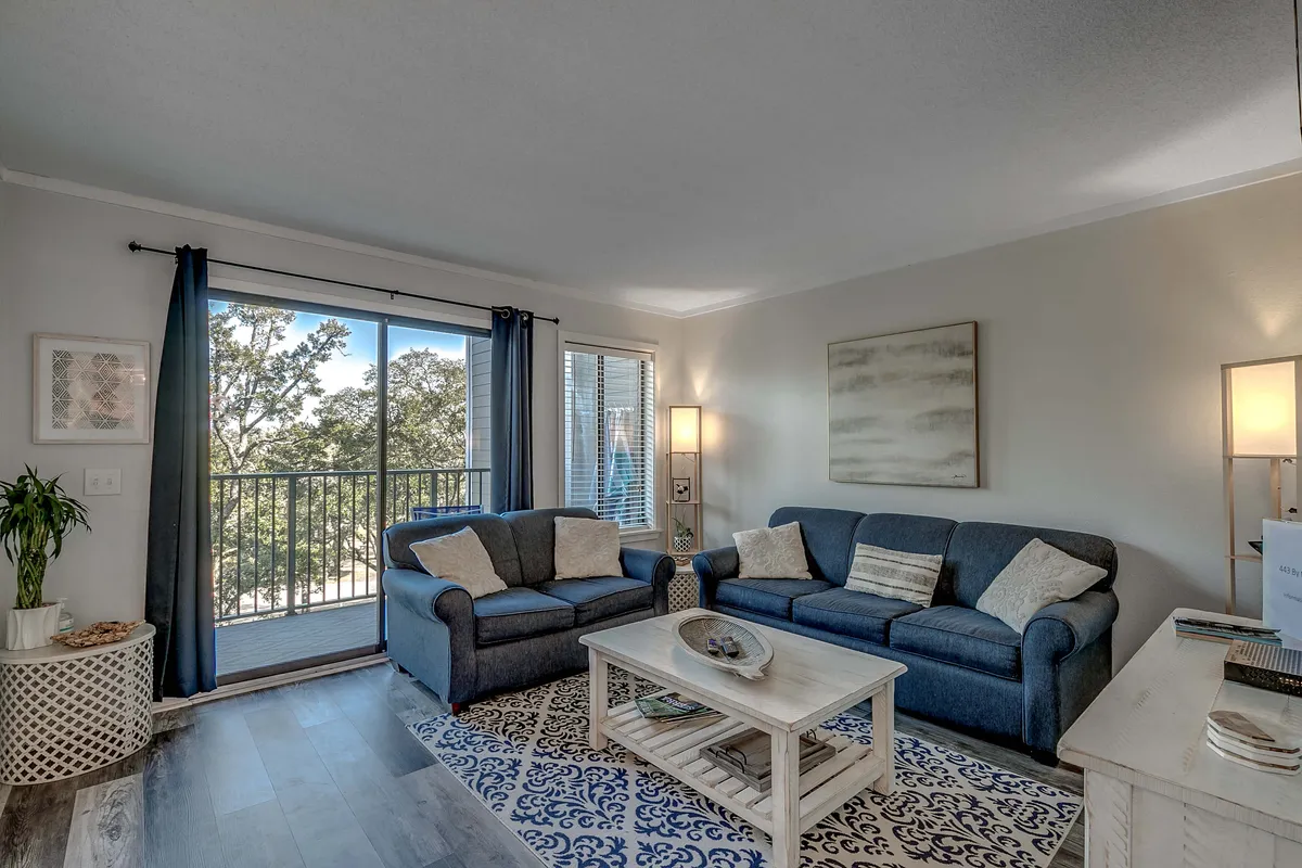 This image displays a comfortable living room setting featuring a plush sofa, coffee table, and a view toward the balcony. Warm lighting and cozy seating invite relaxation and socializing, with the balcony view hinting at openness and natural light.