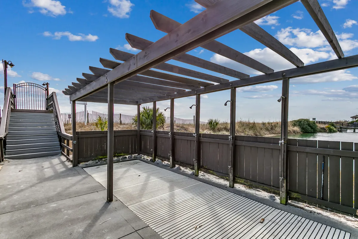 An inviting outdoor pergola set amidst lush vegetation with views of water, a staircase, and open shade, creating an ideal space for gatherings, picnics, or relaxed meals outside. The ambiance is leisurely and perfect for socializing or unwinding with friends and family.
