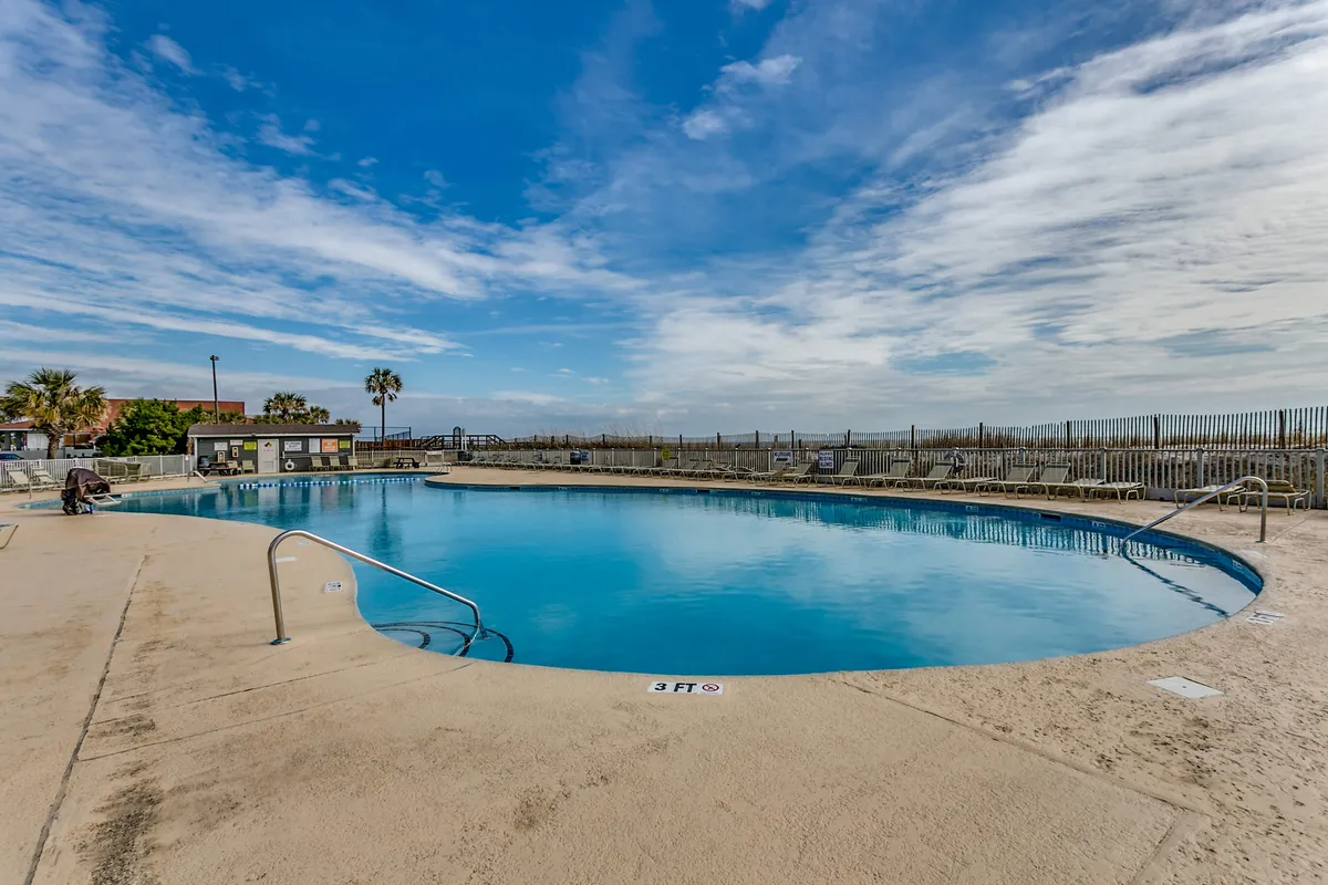An inviting outdoor pool surrounded by lush palm trees and set under a clear blue sky. Lounge chairs are arranged around the pool, offering plenty of spots to relax and enjoy the sun. The overall setting radiates a vacation-like, resort atmosphere.