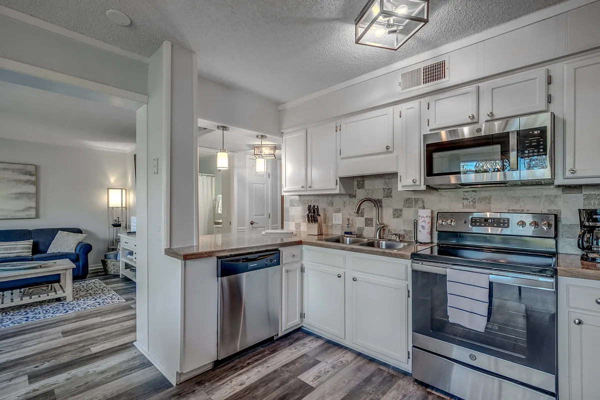 A modern kitchen scene showcasing stainless steel appliances, a spacious countertop, under-cabinet lighting, and contemporary pendant lights. The layout is open and functional, suited for cooking and gathering.